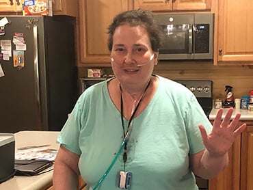 Judy standing in her kitchen raising her hand