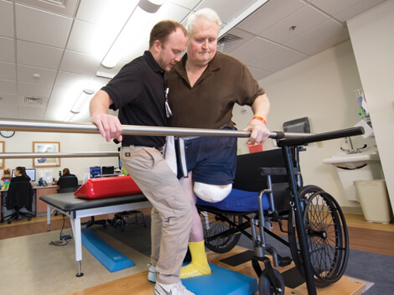 A therapist assists an amputee patient with walking exercises using a parallel bar.