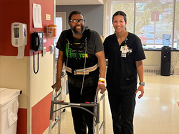 Cory Reeves walks with a walker and his therapist.